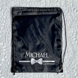 May include: Black drawstring bag with a white bow tie and the text "MICHAEL GROOMSMAN" printed on it.