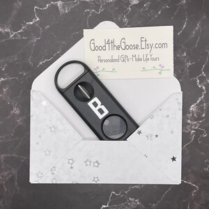 May include: A black cigar cutter with a silver letter "B" on the side, inside a white envelope with silver stars. The envelope has the text "Good4theGoose.Etsy.com" and "Personalized Gifts - Make Life Yours" on a small card inside.