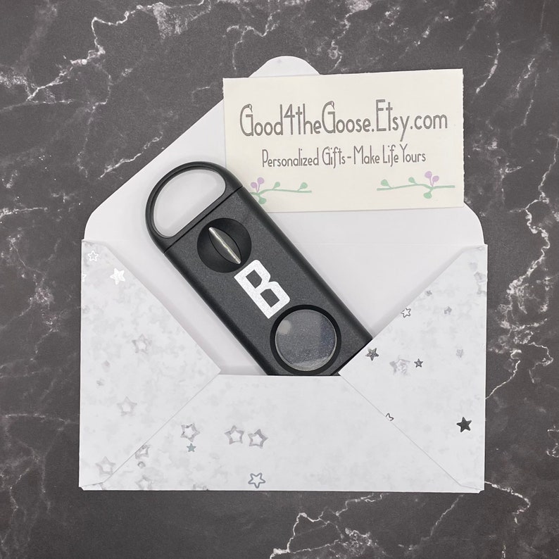 May include: A black cigar cutter with a silver letter "B" on the side, inside a white envelope with silver stars. The envelope has the text "Good4theGoose.Etsy.com" and "Personalized Gifts - Make Life Yours" on a small card inside.