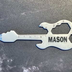 May include: A silver guitar-shaped multi-tool with a ruler on the neck, wrench openings on the body, and the name "MASON" engraved on the body.