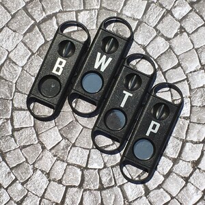 May include: Four black cigar cutters with a circular hole and a small blade. Each cutter has a letter engraved on it: B, W, T, and P.