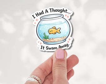 May include: A die-cut sticker featuring a round glass fishbowl with a small orange goldfish, green seaweed, and tan gravel inside. The text "I Had A Thought... It Swam Away." is printed in black above and below the bowl with pink sparkles.