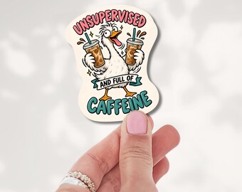 May include: A die-cut sticker featuring a white goose with wide eyes and an open beak, holding two iced coffee cups with teal straws. The text reads UNSUPERVISED at the top in pink and AND FULL OF CAFFEINE at the bottom in teal on a banner.