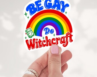 May include: A die-cut sticker featuring a vibrant rainbow arching over the text "Do" and a small green spellbook icon. The blue text "BE GAY" is arched above the rainbow, and the red text "WITCHCRAFT" is curved below, accented by small green stars.