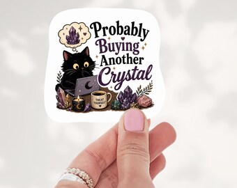 May include: A square sticker featuring a black cat using a laptop, surrounded by crystals, a candle, and a mug labeled "TREAT YOURSELF." The text reads "Probably Buying Another Crystal" with a thought bubble showing a purple crystal cluster.