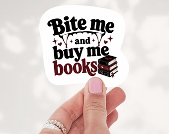 May include: A white die-cut sticker featuring the black text Bite me and buy me books with vampire fangs dripping blood, small red hearts, and a stack of three books with dark covers and a small bat icon on the top book cover.