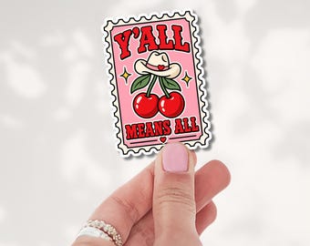 May include: A rectangular sticker shaped like a postage stamp with a pink background. It features two red cherries topped with a white cowboy hat and the red text Y'ALL MEANS ALL. The design includes small yellow stars and a tiny red heart.