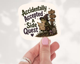 May include: A die-cut sticker featuring a green frog wearing a purple wizard hat and cape, holding a map labeled 'Probably Nothing Important'. Text reads 'Accidentally Accepted A Side Quest'. A wooden signpost points to 'Mysterious Ruins', 'Haunted Forest', and 'Sus'.