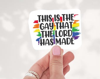 May include: A rectangular sticker with a white background featuring a horizontal rainbow-colored brushstroke design. The black text reads, "THIS IS THE GAY THAT THE LORD HAS MADE," centered in a bold, sans-serif font across the rainbow graphic.