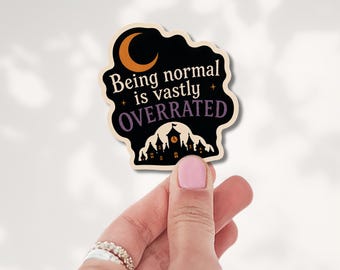 May include: A die-cut sticker with a black background featuring an orange crescent moon, a silhouette of a castle, and the text "Being normal is vastly OVERRATED" in white and purple lettering with small star accents.