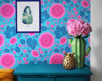 May include: A vibrant interior scene featuring a teal dresser, a framed botanical print, and a cactus-shaped vase holding pink flowers. The background showcases a floral wallpaper with large pink blooms and blue leaves.