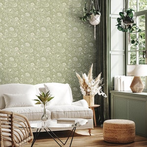 May include: A living room featuring a white sofa, a wicker armchair, a glass coffee table, a potted plant, a woven basket filled with dried flowers, and a woven footstool. The walls are adorned with a green wallpaper featuring a white floral design.