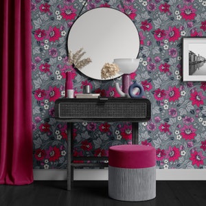 May include: A black vanity table with a woven rattan drawer and a round mirror. The table has a pink velvet stool and is set against a grey floral wallpaper with pink flowers.