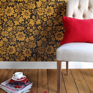 May include: A white chair with a red pillow sits in front of a black and gold floral wallpaper. A stack of magazines and a white cup with red berries are on the wooden floor.