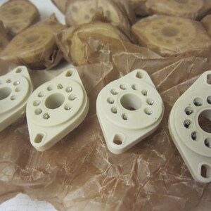 May include: Four white ceramic valve bases with eight metal pins each. The bases are on a brown paper background.