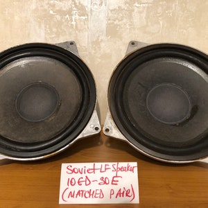 Pode incluir: Dois alto-falantes LF soviéticos 10GD-30E de cor prateada, um par combinado, com bordas de borracha preta. Os alto-falantes estão sobre uma superfície de madeira com uma nota manuscrita vermelha que diz "Soviet LF Speaker 10GD-30E (MATCHED PAIR)".