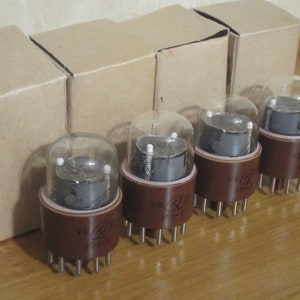 May include: Four vintage vacuum tubes with brown bases and glass enclosures. The tubes are labeled "VI 711", "VI 711", "VI 711", and "VI 711". The tubes are sitting on a wooden surface.