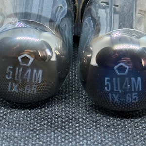 May include: Two glass vacuum tubes featuring a dark, reflective finish. Each tube is marked with a pentagon symbol above the text 5Ц4M and IX-65 printed in white. The internal metal components are visible through the clear glass top section.