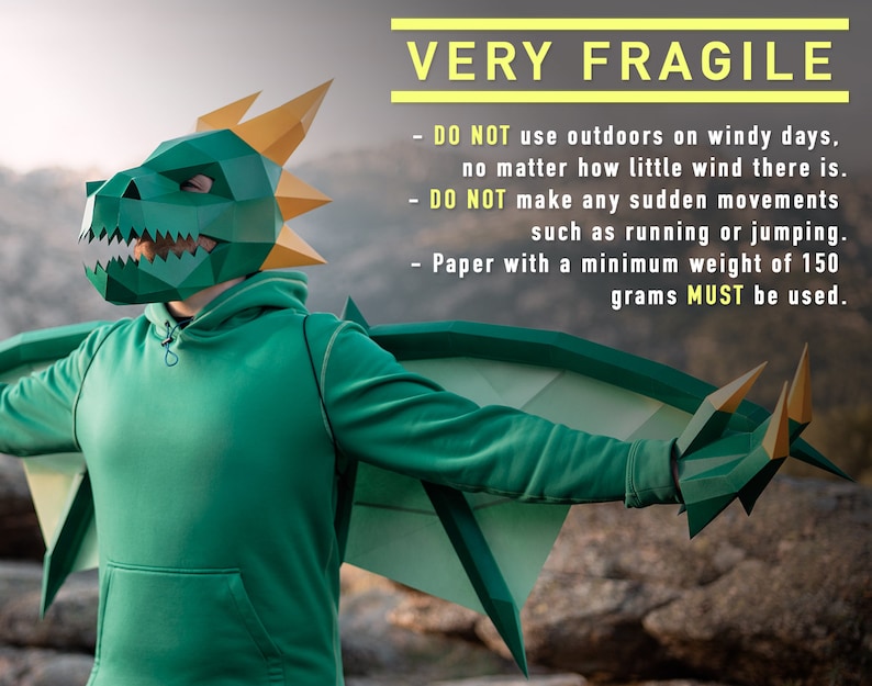 May include: A person wearing a green dragon costume with wings and a mask. The costume is made of paper and is very fragile. The text on the image reads: "VERY FRAGILE - DO NOT use outdoors on windy days, no matter how little wind there is. - DO NOT make any sudden movements such as running or jumping. - Paper with a minimum weight of 150 grams MUST be used."