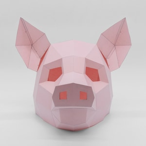 K&ouml;nnte beinhalten: Eine rosa Papierkunst-Schweinemaske mit einem 3D-Design. Die Maske hat eine Schnauze, Augen und Ohren.