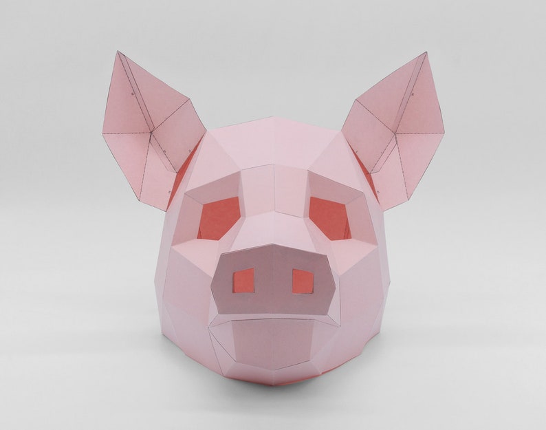 K&ouml;nnte beinhalten: Eine rosa Papierkunst-Schweinemaske mit einem 3D-Design. Die Maske hat eine Schnauze, Augen und Ohren.