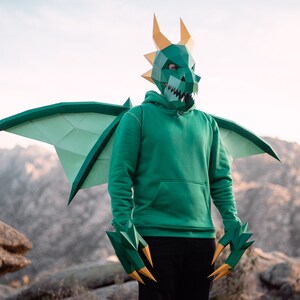 May include: A person wearing a green dragon costume with wings and claws. The costume is made of paper and has a realistic design.