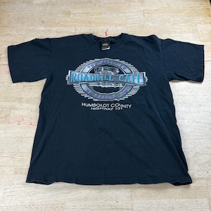 Könnte beinhalten: Schwarzes T-Shirt mit einem kreisförmigen Aufdruck mit der Aufschrift "Roadkill Cafe" in einer stilisierten Schriftart. Die Grafik enthält ein Bild eines Autos und den Text "Humboldt County Highway 101". Das Shirt ist aus weichem Material.