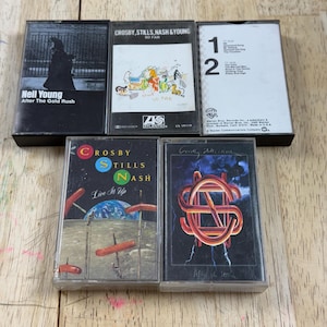 Könnte beinhalten: Sammlung von Vintage-Kassetten mit Albumcovern von Neil Young, Crosby, Stills, Nash & Young. Die Kassetten zeigen Albumtitel wie "After The Gold Rush", "So Far" und "Live It Up". Die Kassettenhüllen sind schwarz und weiß.