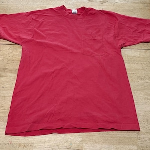 Könnte beinhalten: Ein rotes T-Shirt mit einer einzigen Tasche auf der linken Seite.