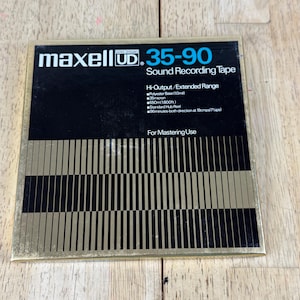 May include: A square Maxell UD 35-90 sound recording tape box with a black and gold striped design. The text reads Maxell UD 35-90 Sound Recording Tape, Hi-Output/Extended Range, Polyester Base 1.0mil, 35micron, 550m 1800ft, Standard Hub Reel, 96minutes.