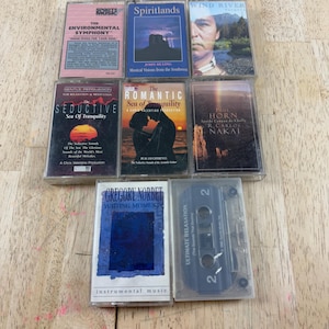 May include: A selection of vintage cassette tapes, each with unique album art. Titles visible include "The Environmental Symphony," "Spiritlands," and "Wind River." The tapes are displayed on a wooden surface. The collection offers a nostalgic feel.