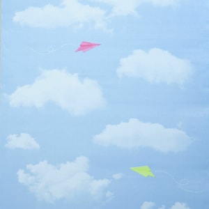 Op de afbeelding: Twee papieren vliegtuigjes vliegen in een blauwe lucht met witte wolken. Het bovenste vliegtuigje is roze en het onderste vliegtuigje is groen.