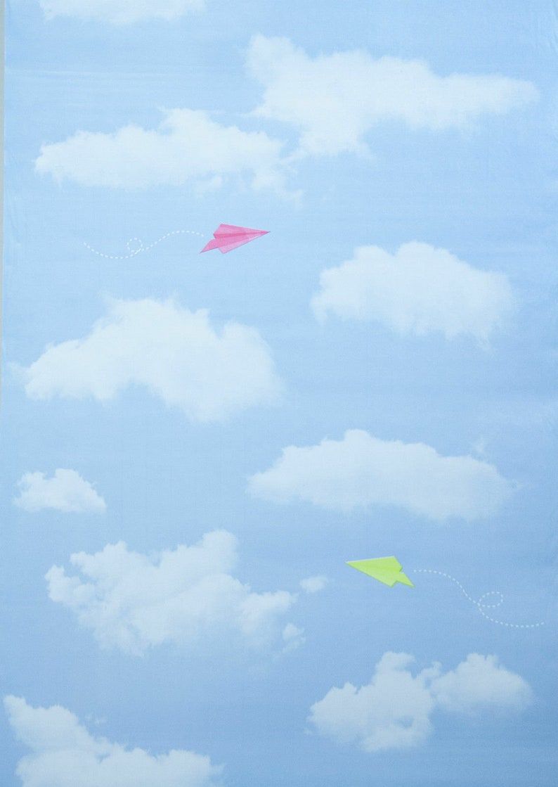 Op de afbeelding: Twee papieren vliegtuigjes vliegen in een blauwe lucht met witte wolken. Het bovenste vliegtuigje is roze en het onderste vliegtuigje is groen.
