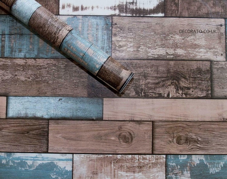 May include: A roll of wood-look self-adhesive wallpaper with a rustic, weathered design. The wallpaper features a mix of brown and blue tones, creating a realistic wood plank effect. The roll is partially unrolled, revealing the adhesive backing.