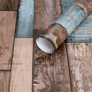 May include: A roll of wood-look self-adhesive wallpaper with a rustic, weathered design. The wallpaper features a mix of brown and blue tones, creating a realistic wood plank effect. The text "DECORATO-CO-UK" is printed on the wallpaper.