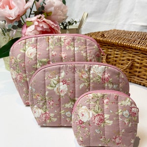 Op de afbeelding: Drie roze quilted ritszakjes met een bloemenprint. De zakjes zijn in elkaar genest, met het grootste zakje onderaan en het kleinste zakje bovenaan.