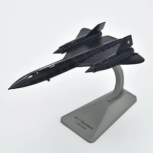 Puede incluir: Una taza de cerámica blanca con un asa negra y el texto "But First, Coffee" en negro, con una fuente de estilo manuscrito. La taza está sobre una superficie blanca.