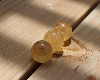 May include: Four smooth, golden yellow crystal spheres arranged in a row on a wooden surface.