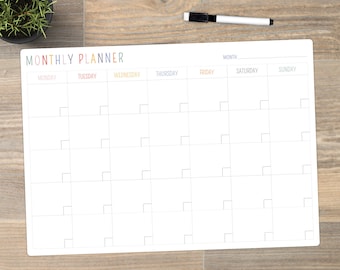 May include: A white monthly planner with a grid layout for scheduling. The title "MONTHLY PLANNER" is in colorful letters. Days of the week are listed across the top in different colors. A black and white marker is on the top right.