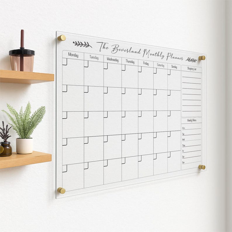 May include: A clear acrylic monthly planner with gold-colored hardware. The planner features a grid layout for each day of the month, with the days of the week labeled across the top. The text "The Beversland Monthly Planner" is printed at the top.
