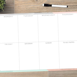 May include: A white weekly planner with sections for each day of the week, including "To Do / Notes." The planner has a light blue and rose gold border. A black and white dry-erase marker is on the top right.
