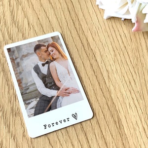 May include: A white rectangular photo card with a picture of a couple. The photo card has a black heart and the word "Forever" printed at the bottom. The background is a light wood surface.