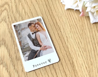 May include: A white rectangular photo card with a picture of a couple. The photo card has a black heart and the word "Forever" printed at the bottom. The background is a light wood surface.