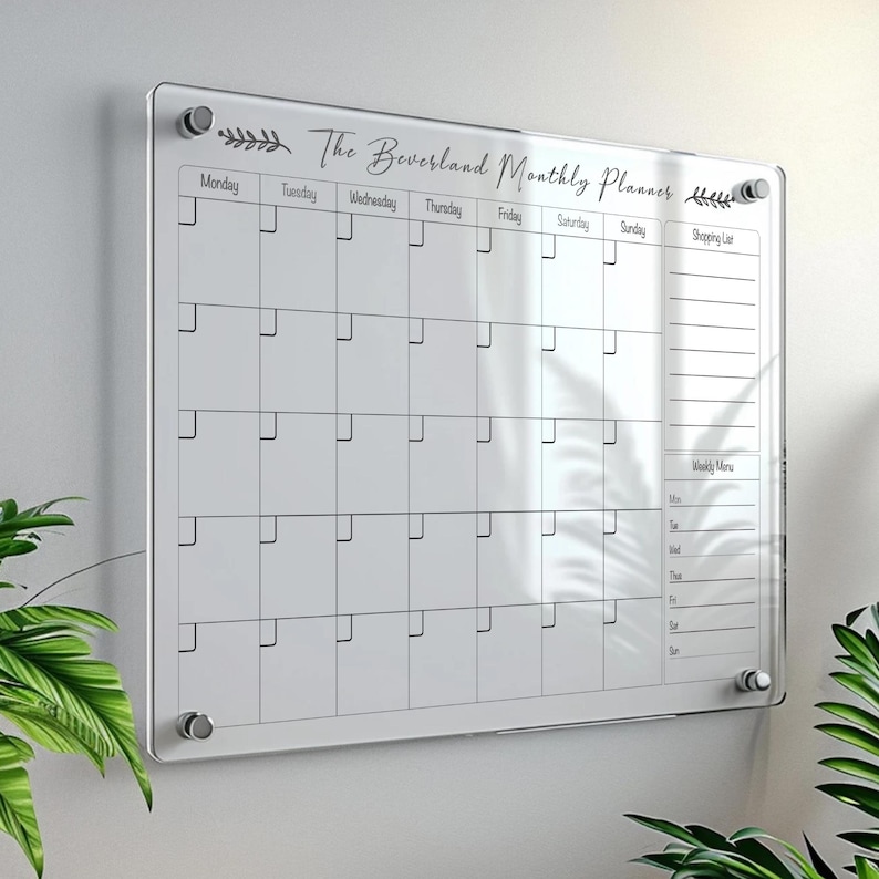May include: A clear acrylic monthly planner with the text "The Beversland Monthly Planner" and a grid layout for scheduling. Includes a shopping list and weekly menu sections. Mounted on a wall with silver hardware.
