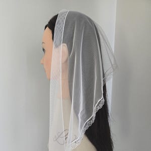 May include: A white, sheer veil with a delicate lace trim. The veil is draped over a mannequin head with dark hair, showcasing its elegant design. The lace trim adds a touch of sophistication to this bridal or formal accessory.