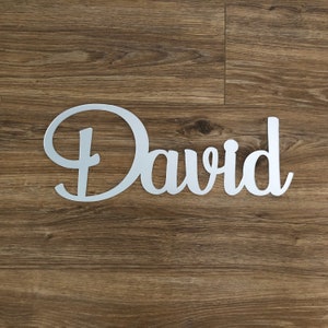 Puede incluir: Un letrero de nombre de metal plateado con el nombre "David" escrito en letra cursiva.