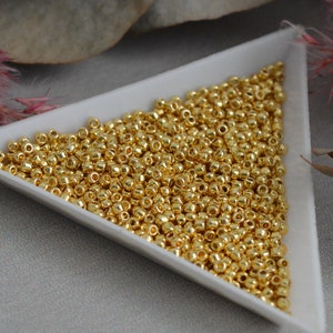 May include: A white triangular dish filled with gold-coloured round beads.
