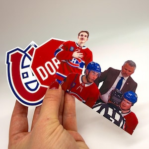 Op de afbeelding: Een verzameling gestanste stickers met ijshockeyafbeeldingen van de Montreal Canadiens, waaronder een rood en blauw teamlogo, een rood stopbord met de tekst DOR en diverse foto's van ijshockeyers en een coach in pak.