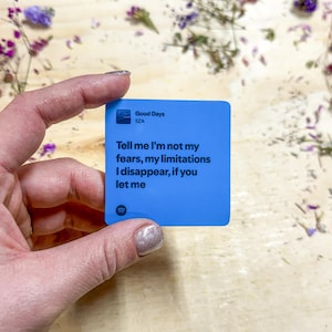 Op de afbeelding: Een blauwe vierkante sticker met de tekst "Good Days" van SZA. De sticker bevat ook de tekst "Tell me I'm not my fears, my limitations I disappear, if you let me."