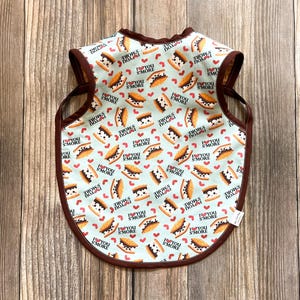 May include: A light blue bib with a brown trim featuring a repeating pattern of s'mores and hearts with the text "I love you s'more".